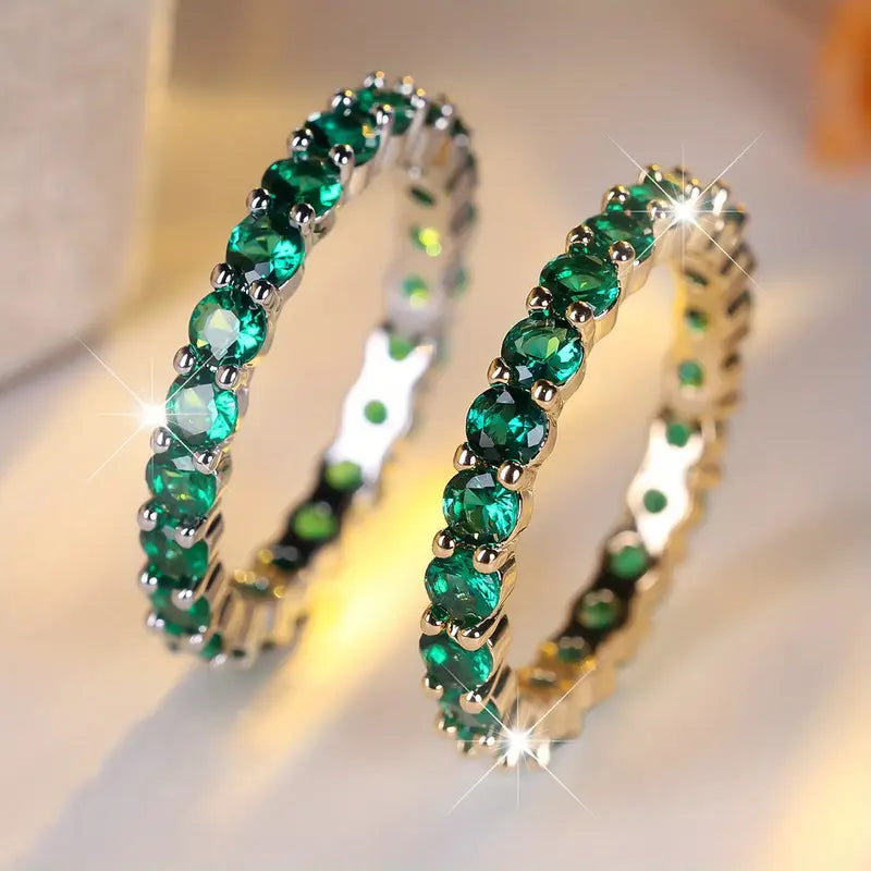 Zwei goldene Ringe mit grünen ovalen Steinen, jeweils mit goldener Fassung