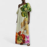 Maxikleid mit Blumendruck und schrägem Ausschnitt, cremefarben mit großen grünen und orangefarbenen Blumen.