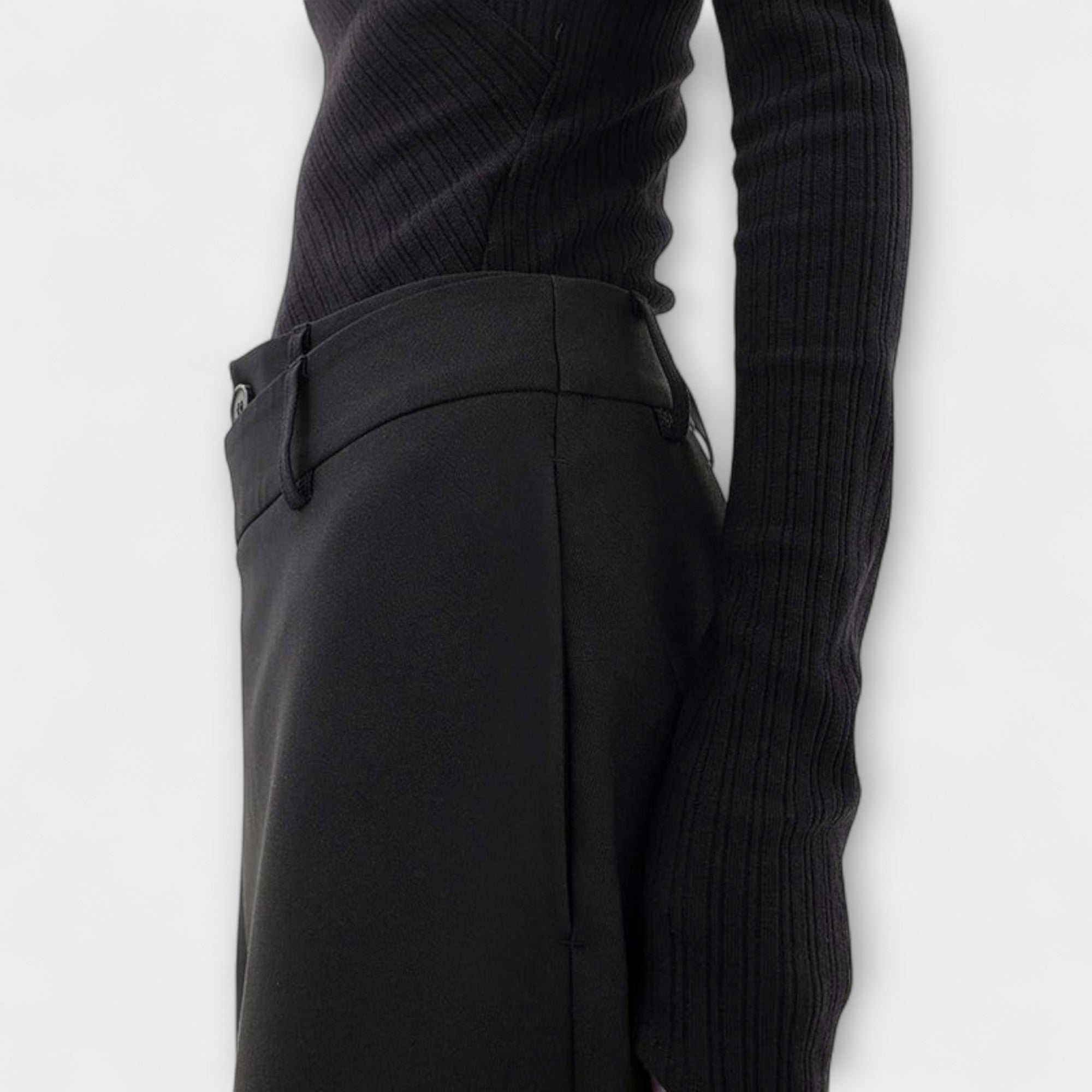 Asymmetrische Hose in Schwarz: Detail am Bund mit Knopf und schmalem Seitendetail.