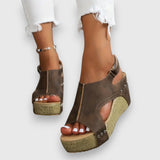 Plateau-Sandalen mit Knöchelriemen, Nieten und Kork-Optiksohle, dunkelbraun, offene Zehen.
