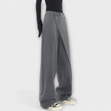 Asymmetrische Hose in Grau mit weitem Bein und Drapierung, Knopf am Bund sichtbar.