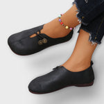 Schwarze Slipper mit Schnürriemen und goldfarbenen Zierknöpfen am Obermaterial